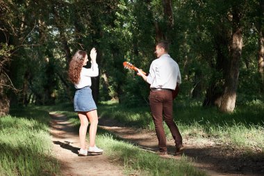 Genç çift, ormanda yürüyüş gitar çalmak ve dans, yaz doğa, parlak güneş ışığı, gölgeler ve yeşil yaprakları, romantik duygular