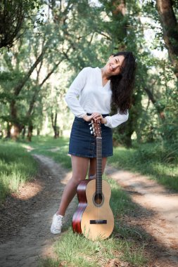 ormanda yürüyüş ve iskambil gitar, yaz doğa, parlak güneş ışığı, gölgeler ve yeşil yaprakları, romantik duygular genç kadın