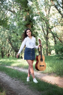 ormanda yürüyüş ve iskambil gitar, yaz doğa, parlak güneş ışığı, gölgeler ve yeşil yaprakları, romantik duygular genç kadın