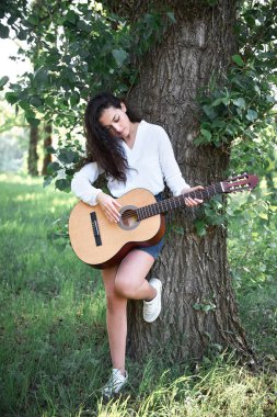 ormanda yürüyüş ve iskambil gitar, yaz doğa, parlak güneş ışığı, gölgeler ve yeşil yaprakları, romantik duygular genç kadın