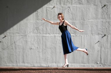 Genç kız bir beton duvara poz giyinmiş siyah, sert ışık ve gölge