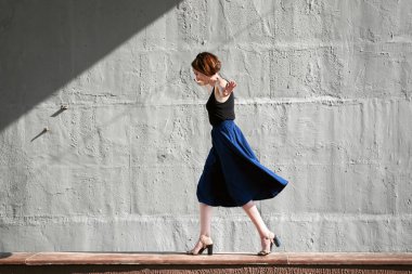 Genç kız bir beton duvara poz giyinmiş siyah, sert ışık ve gölge