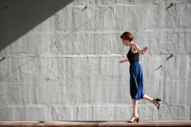 Genç kız bir beton duvara poz giyinmiş siyah, sert ışık ve gölge