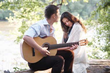Genç çift, bir günlük nehrin yanında oturan ve iskambil gitar, yaz doğa, parlak güneş ışığı gölgeler ve yeşil yaprakları, romantik duygular