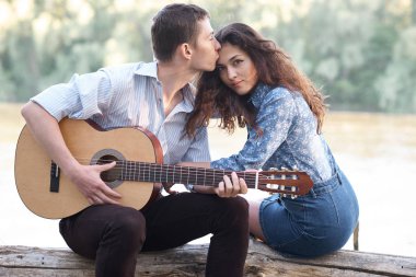 Genç çift, bir günlük nehrin yanında oturan ve iskambil gitar, yaz doğa, parlak güneş ışığı gölgeler ve yeşil yaprakları, romantik duygular