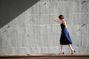 Genç kız bir beton duvara poz giyinmiş siyah, sert ışık ve gölge