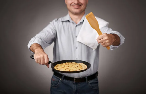 man posing with a pancake in a pan, white shirt and pants, gray background, shallow depth of field, sharp pancake and blurred face