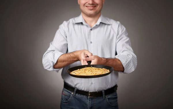 man posing with a pancake in a pan, white shirt and pants, gray background, shallow depth of field, sharp pancake and blurred face