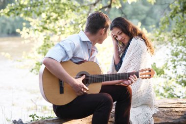 Genç çift, bir günlük nehrin yanında oturan ve iskambil gitar, yaz doğa, parlak güneş ışığı gölgeler ve yeşil yaprakları, romantik duygular