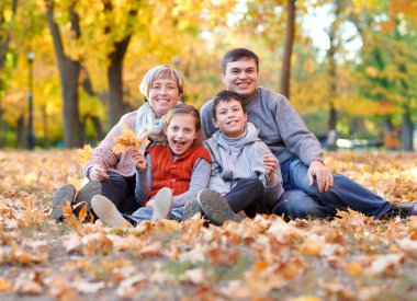 Mutlu aile sonbahar Şehir Parkı düşen yapraklar üzerinde yer almaktadır. Çocuklar ve ebeveynler poz, gülümseyen, oyun ve eğlenmek. Parlak sarı ağaçlar.