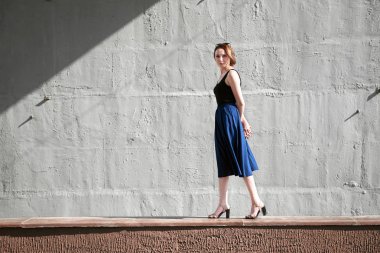 Genç kız bir beton duvara poz giyinmiş siyah, sert ışık ve gölge