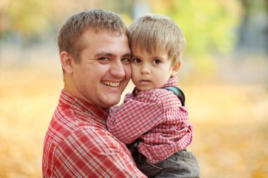 Baba ve oğul oynama ve sonbahar şehir parkında eğleniyor. Poz, gülüyor, oynuyor. Parlak sarı ağaçlar.