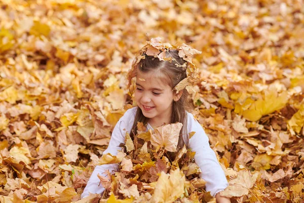 子供の女の子が横になっていると秋の市公園で落ち葉で遊んで — ストック写真