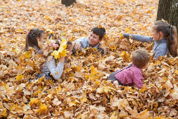 在秋天的城市公园里 孩子们躺在落叶上玩耍 — 图库照片