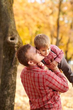 Baba çocuk yüksek rütbeli atar. Baba ve oğul oynama ve sonbahar şehir parkında eğleniyor. Poz, gülüyor, oynuyor. Parlak sarı ağaçlar.