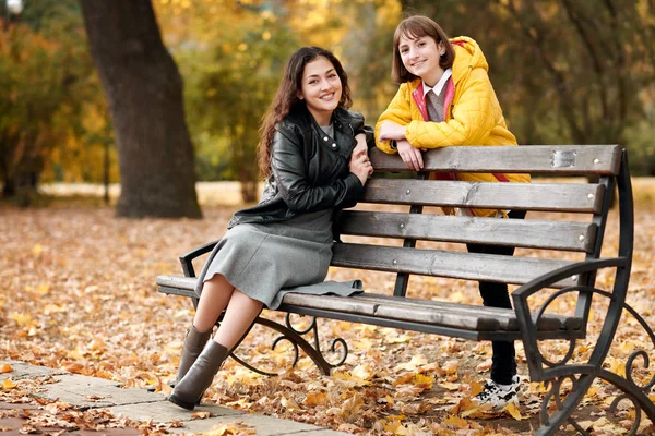 两个女孩在秋城公园 他们坐在板凳上聊天 — 图库照片