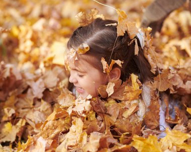 Kız Çocuk yalan ve düşen yapraklar sonbahar şehir parkında oynayan.