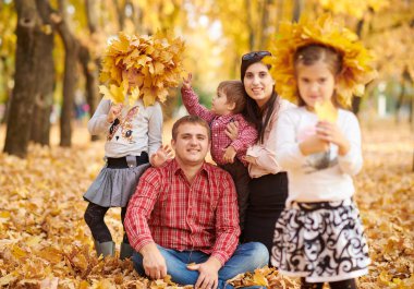 Mutlu aile sonbahar şehir Park'ta oturuyor. Çocuklar ve ebeveynler. Onlar poz, gülümseyen, oyun ve eğlenmek. Parlak sarı ağaçlar.