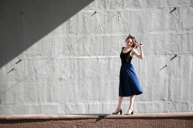 Genç kız bir beton duvara poz giyinmiş siyah, sert ışık ve gölge