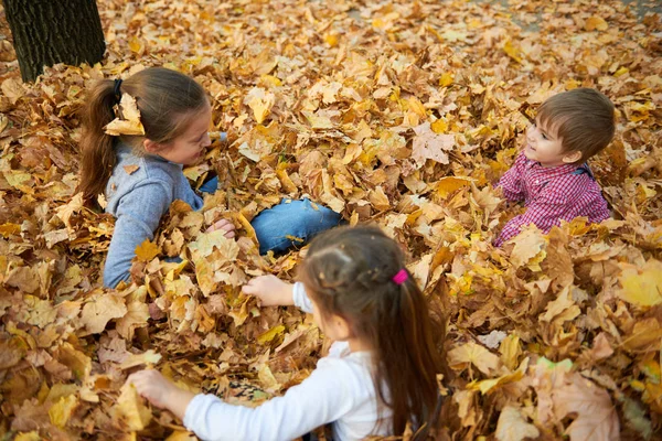 子供が横たわっていると秋の市公園で落ち葉で遊んで — ストック写真