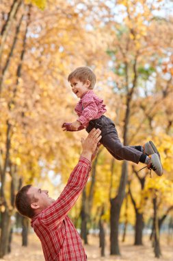 Baba çocuk yüksek rütbeli atar. Baba ve oğul oynama ve sonbahar şehir parkında eğleniyor. Poz, gülüyor, oynuyor. Parlak sarı ağaçlar.