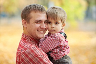 Baba ve oğul oynama ve sonbahar şehir parkında eğleniyor. Poz, gülüyor, oynuyor. Parlak sarı ağaçlar.