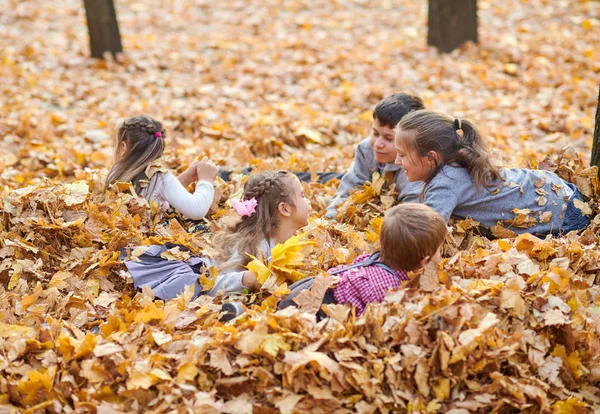 子供が横たわっていると秋の市公園で落ち葉で遊んで — ストック写真