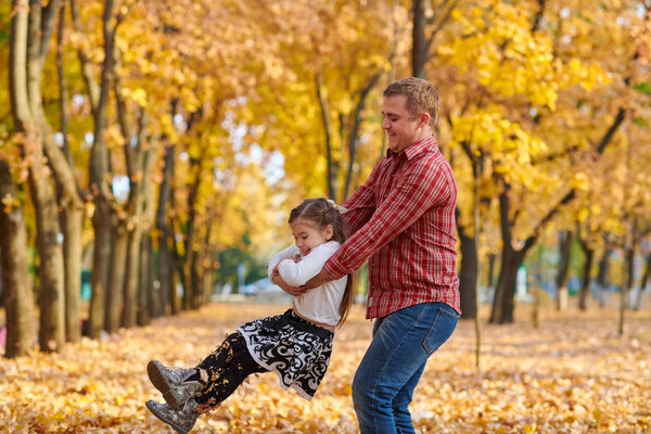 Father and daughter are playing and having fun in autumn city park. They posing, smiling, playing. Bright yellow trees.