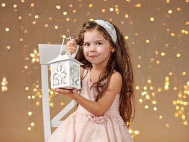 kız çocuk Noel ışıkları, sarı arka plan, pembe elbiseli fenerle poz