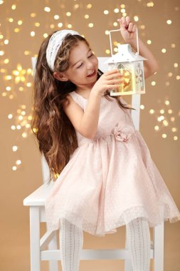 kız çocuk Noel ışıkları, sarı arka plan, pembe elbiseli fenerle poz