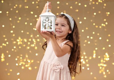 kız çocuk Noel ışıkları, sarı arka plan, pembe elbiseli fenerle poz