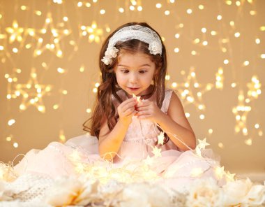 Kız çocuk pembe elbise giymiş sarı arka plan, Noel ışıkları ile oynuyor. Yıldız ışığı bakıyor.