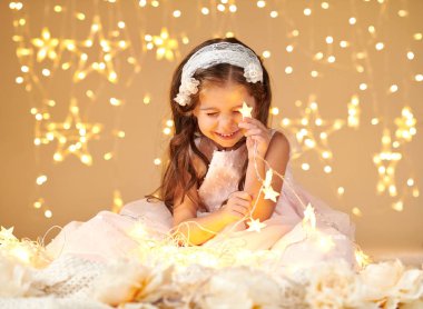 Kız çocuk pembe elbise giymiş sarı arka plan, Noel ışıkları ile oynuyor. Yıldız ışığı bakıyor.