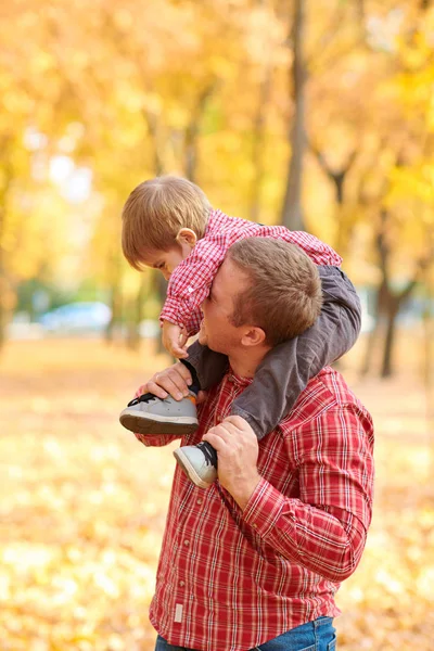 Baba ve oğul oynama ve sonbahar şehir parkında eğleniyor. Poz, gülüyor, oynuyor. Parlak sarı ağaçlar.