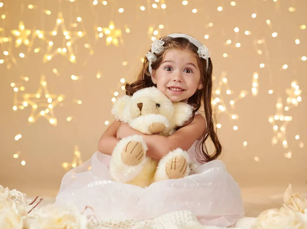 Flickor med björn leksak poserar i christmas lights, gul bakgrund, rosa klänning — Stockfoto