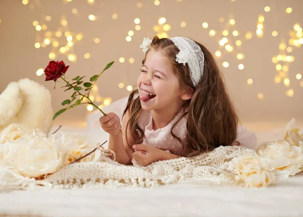 Niña con flor de rosa está posando en luces de Navidad, fondo amarillo, vestido rosa — Foto de Stock