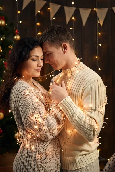 Giovane coppia è in decorazione di Natale e luci, abete su sfondo di legno scuro, concetto di festa di Capodanno — Foto Stock
