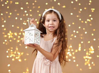 kız çocuk Noel ışıkları, sarı arka plan, pembe elbiseli fenerle poz