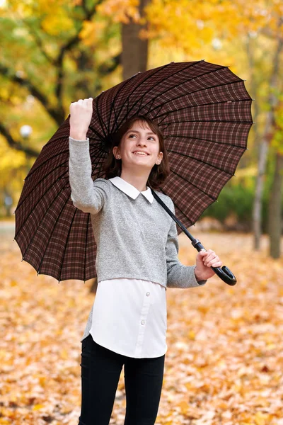 Teenie-Mädchen mit Regenschirm posiert im Herbst Park. leuchtend gelbe Blätter und Bäume. — Stockfoto