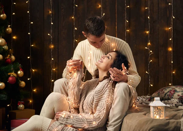 Giovane coppia è in luci di Natale e decorazione, vestito di bianco, abete su sfondo di legno scuro, concetto di vacanza invernale — Foto Stock