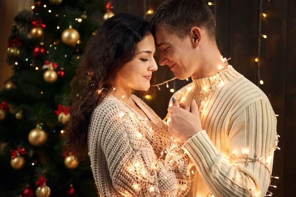 Νεαρό ζευγάρι είναι στην διακόσμηση Χριστουγέννων και φώτων, έλατο σε σκούρο φόντο ξύλινη, νέο έτος διακοπές έννοια — Φωτογραφία Αρχείου