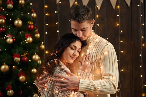 Giovane coppia è in decorazione di Natale e luci, abete su sfondo di legno scuro, concetto di festa di Capodanno — Foto Stock
