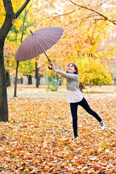 少女与伞摆姿势在秋天的公园 明亮的黄色树叶和树木 她模仿风 — 图库照片