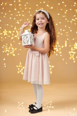 kız çocuk Noel ışıkları, sarı arka plan, pembe elbiseli fenerle poz