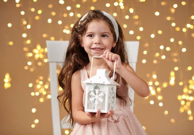 kız çocuk Noel ışıkları, sarı arka plan, pembe elbiseli fenerle poz