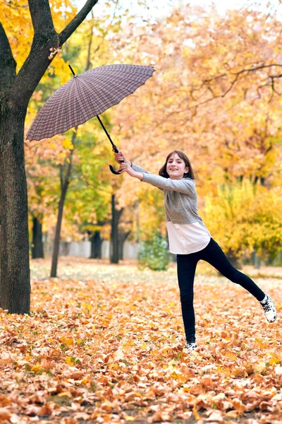 少女与伞摆姿势在秋天的公园 明亮的黄色树叶和树木 她模仿风 — 图库照片