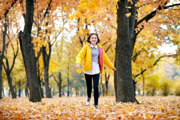 快乐的少女在秋天的公园里和大枫叶们跑着 明亮的黄色叶子和树 — 图库照片