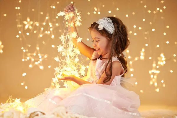 Dívka Dítě Hraje Vánoční Světla Žluté Pozadí Růžové Šaty — Stock fotografie