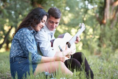 Genç çift ormanda oturan ve iskambil gitar, yaz doğa, parlak güneş ışığı, gölgeler ve yeşil yaprakları, romantik duygular