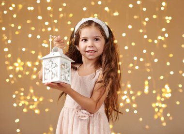 kız çocuk Noel ışıkları, sarı arka plan, pembe elbiseli fenerle poz